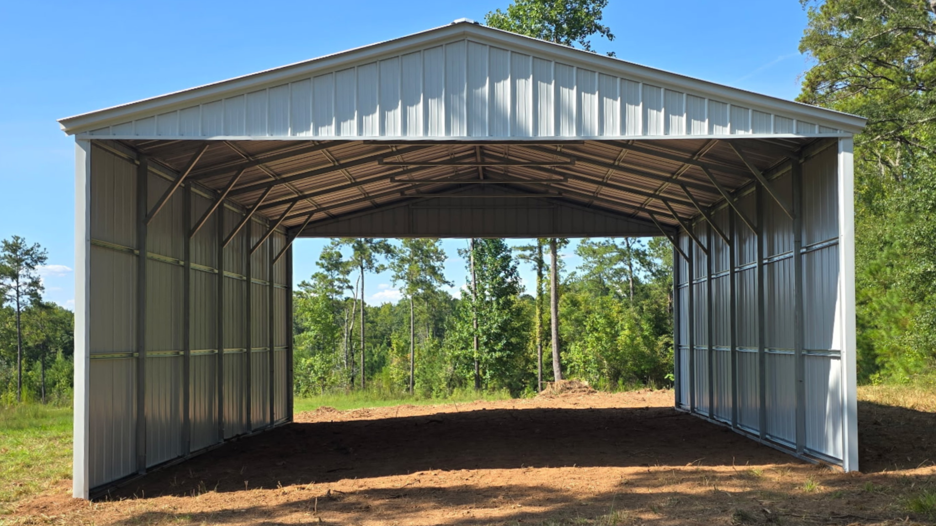 Open-sided metal barn with a peaked roof in a wooded clearing