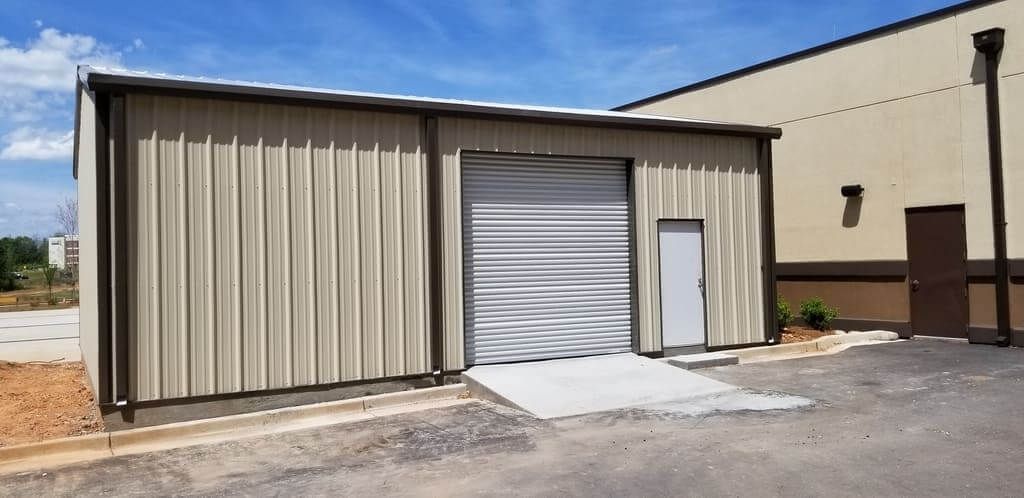 A metal building with a garage door is sitting next to a building.