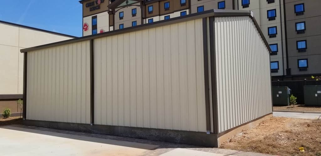 A metal building is sitting on top of a dirt field in front of a building.