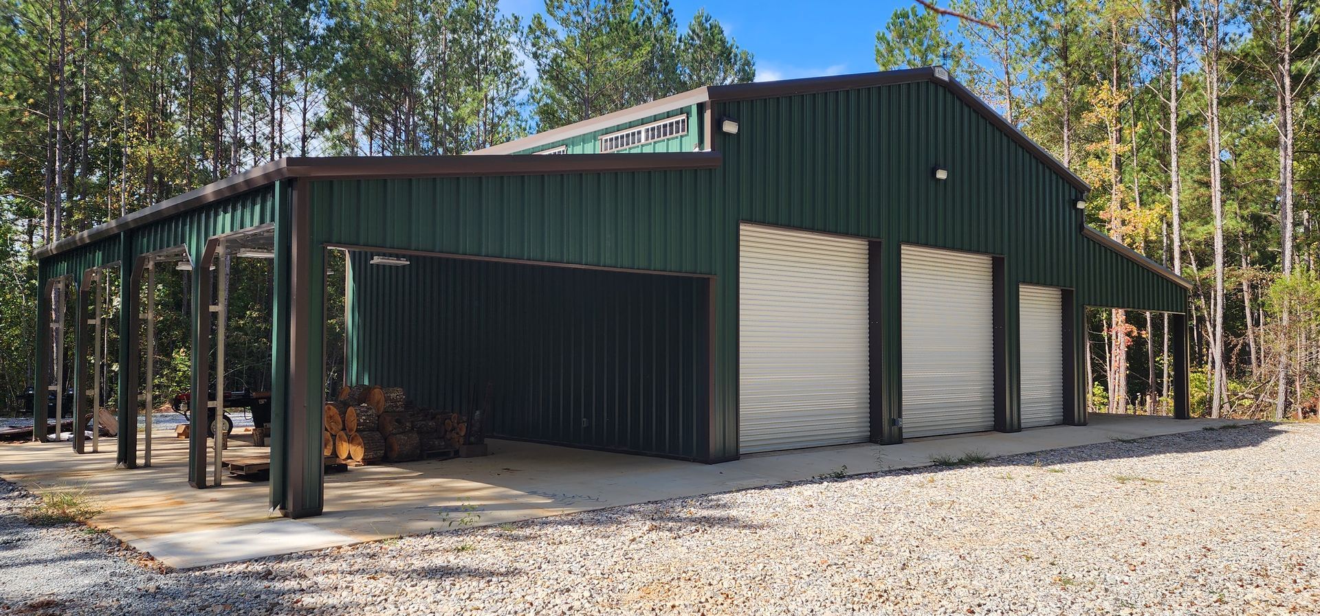 A garage with a carport underneath it is surrounded by trees and gravel.