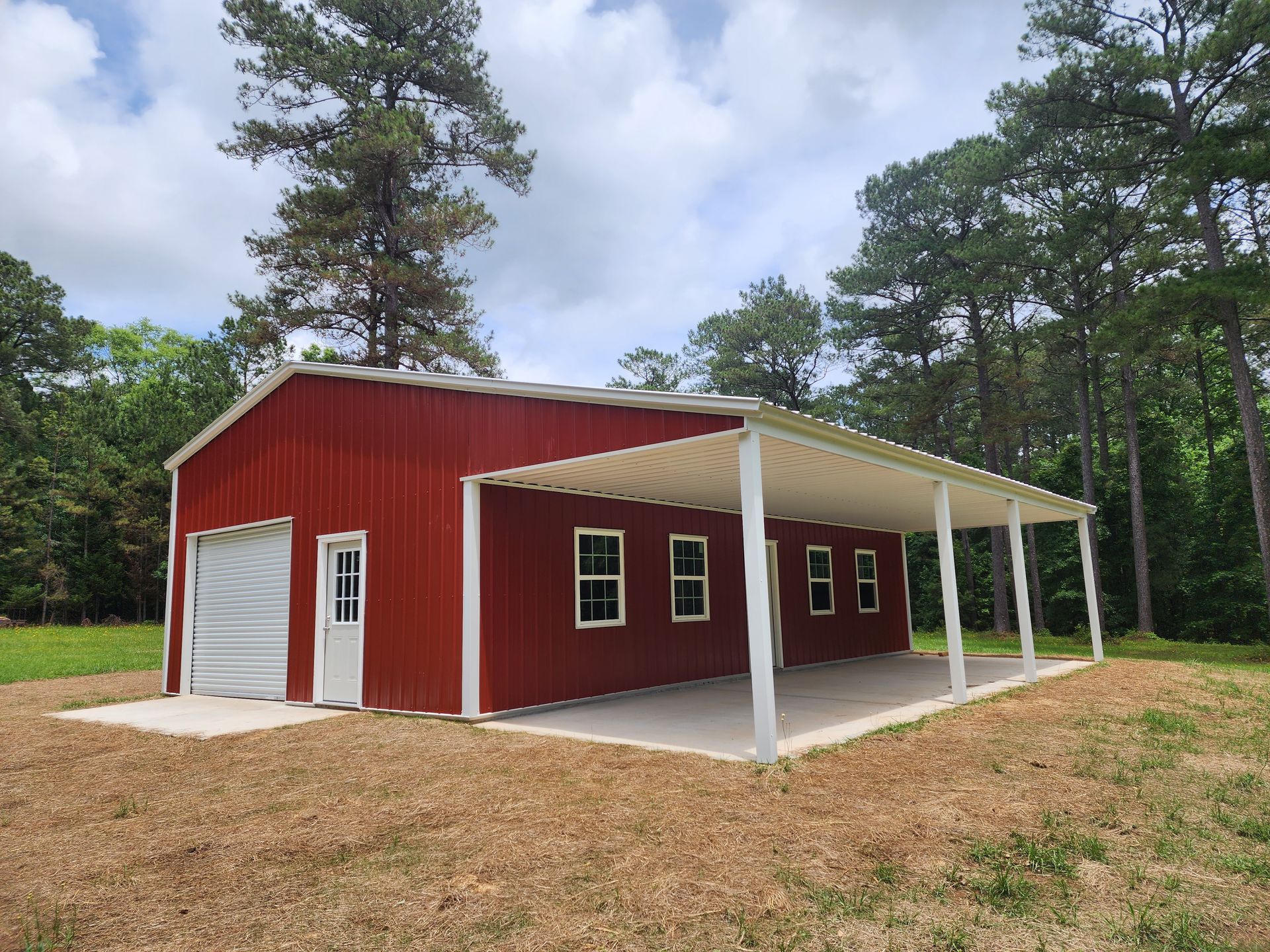 A red barn with a white porch is sitting in the middle of a field.