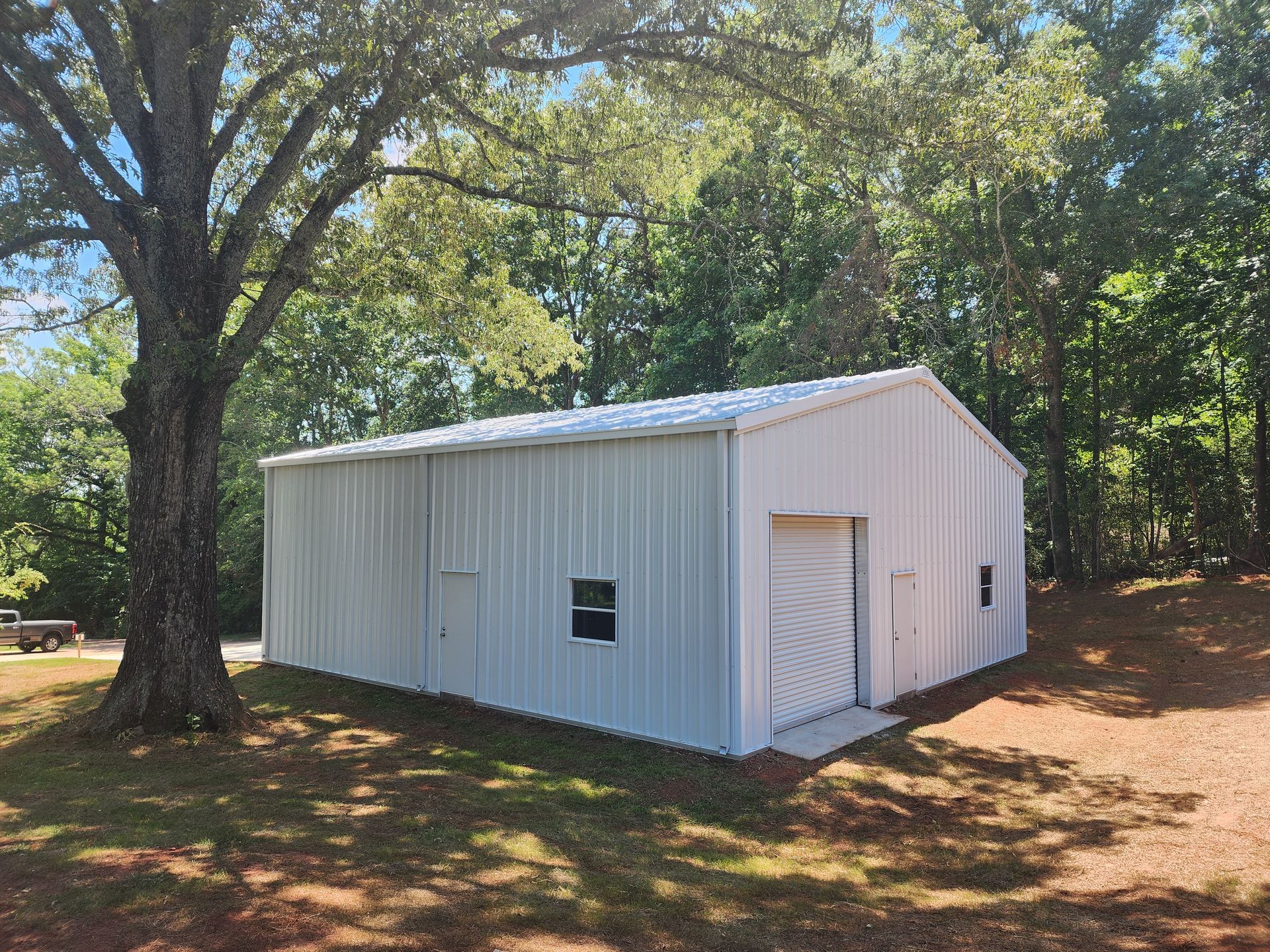 A white metal building is sitting in the middle of a field next to a tree.