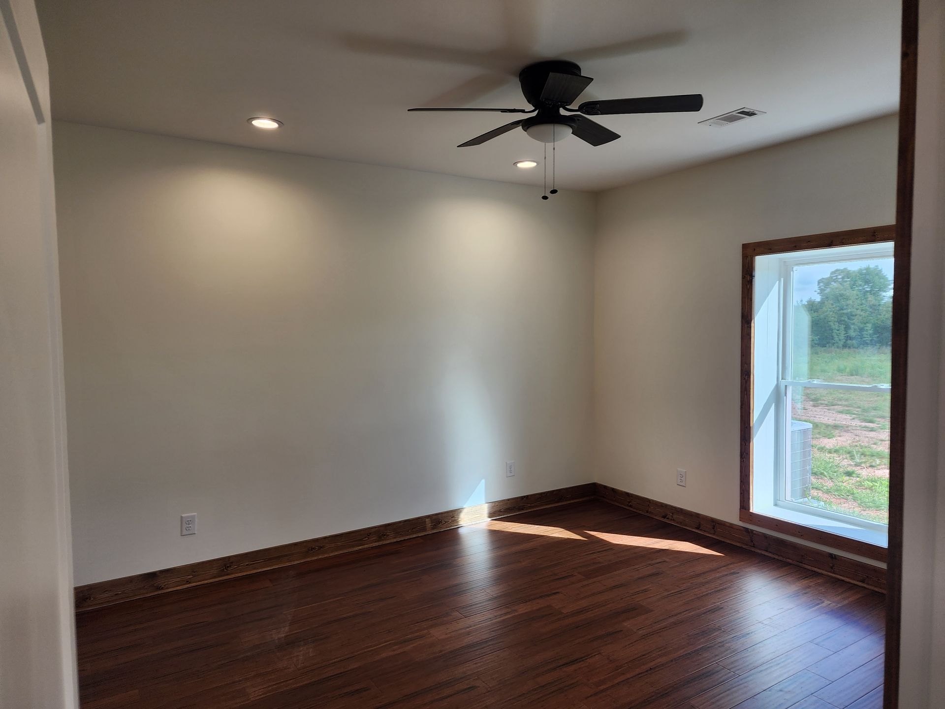 An empty room with a ceiling fan and a window.