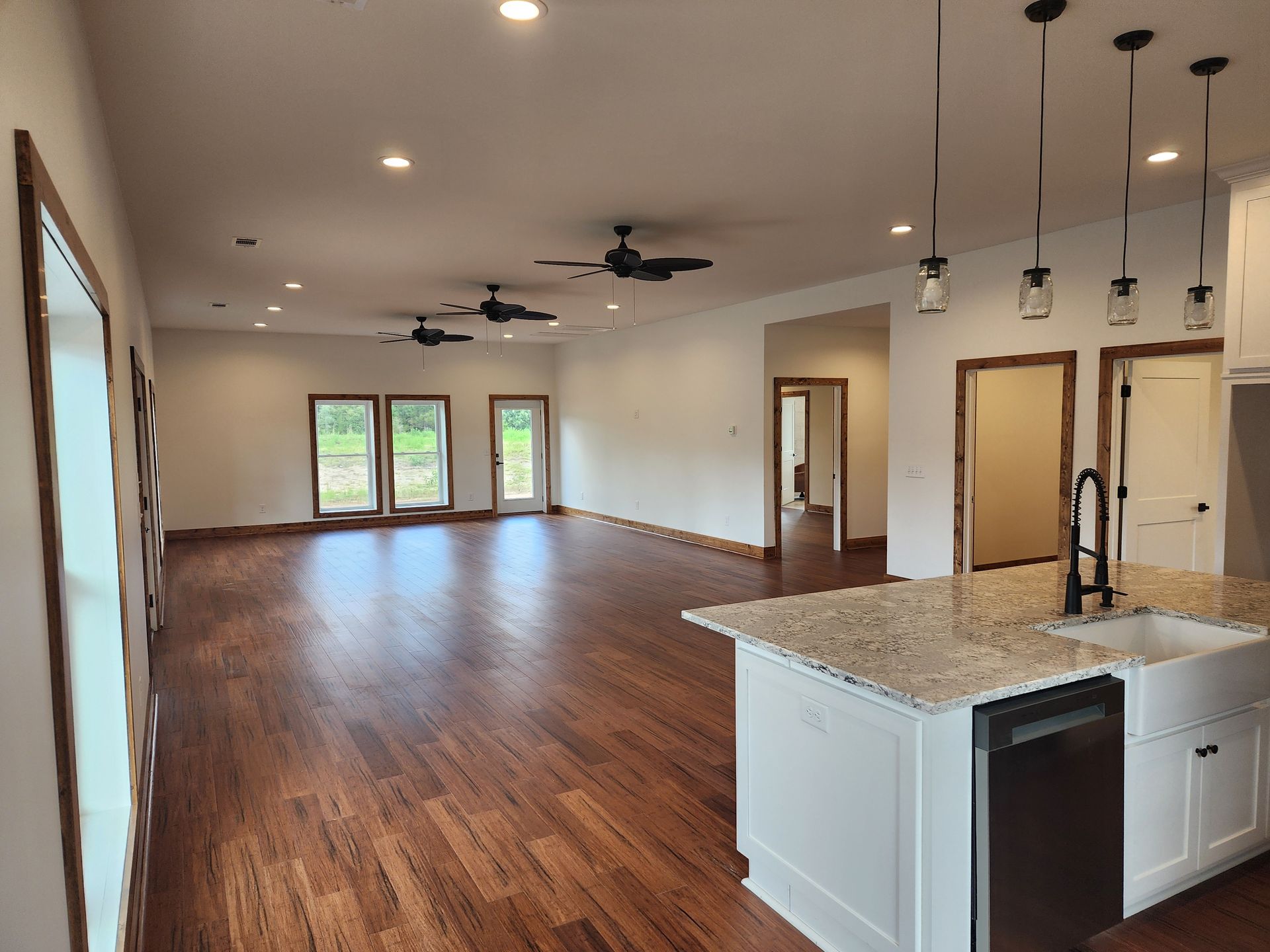 Open-concept living space with hardwood floors, white walls, and a kitchen island with granite countertops.