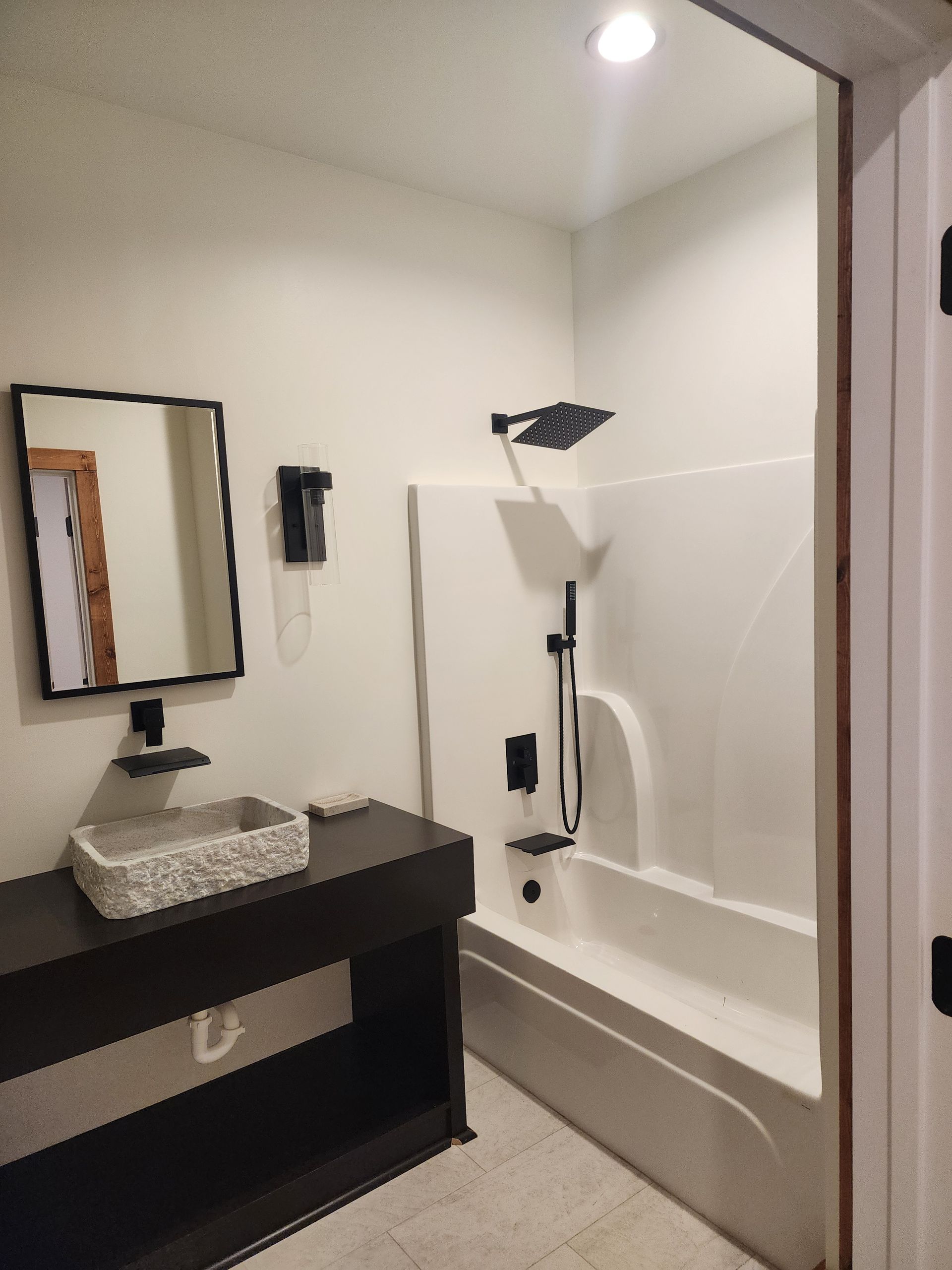 Bathroom with dark vanity, white tub/shower, and black fixtures.
