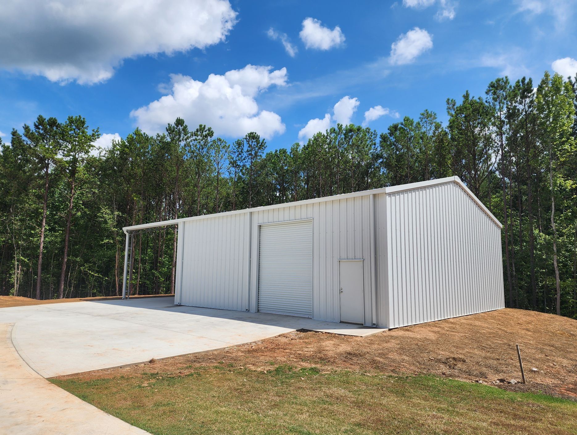 A white metal building with a garage door is sitting in the middle of a grassy field.