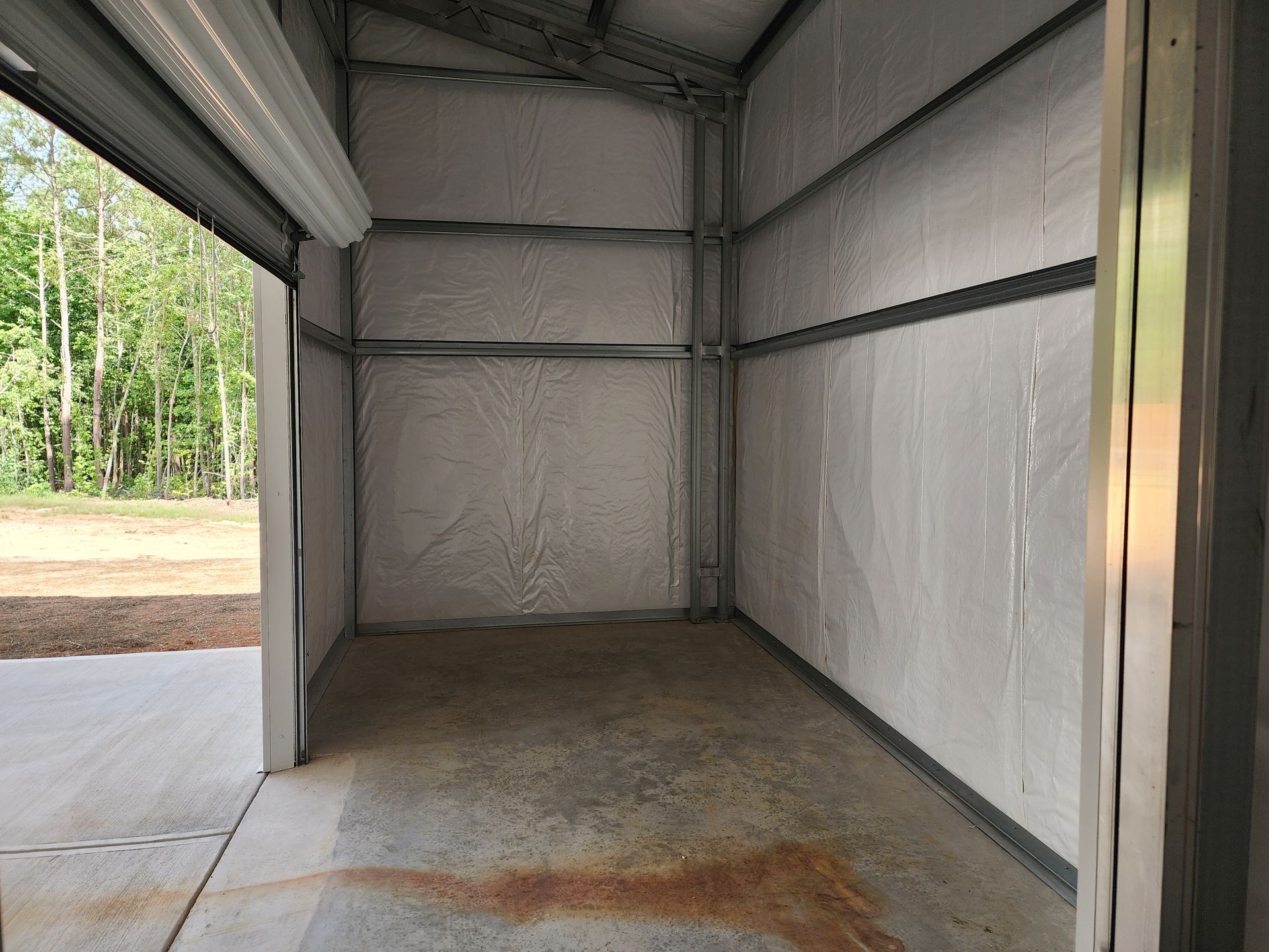 An empty garage with a garage door open and trees in the background.