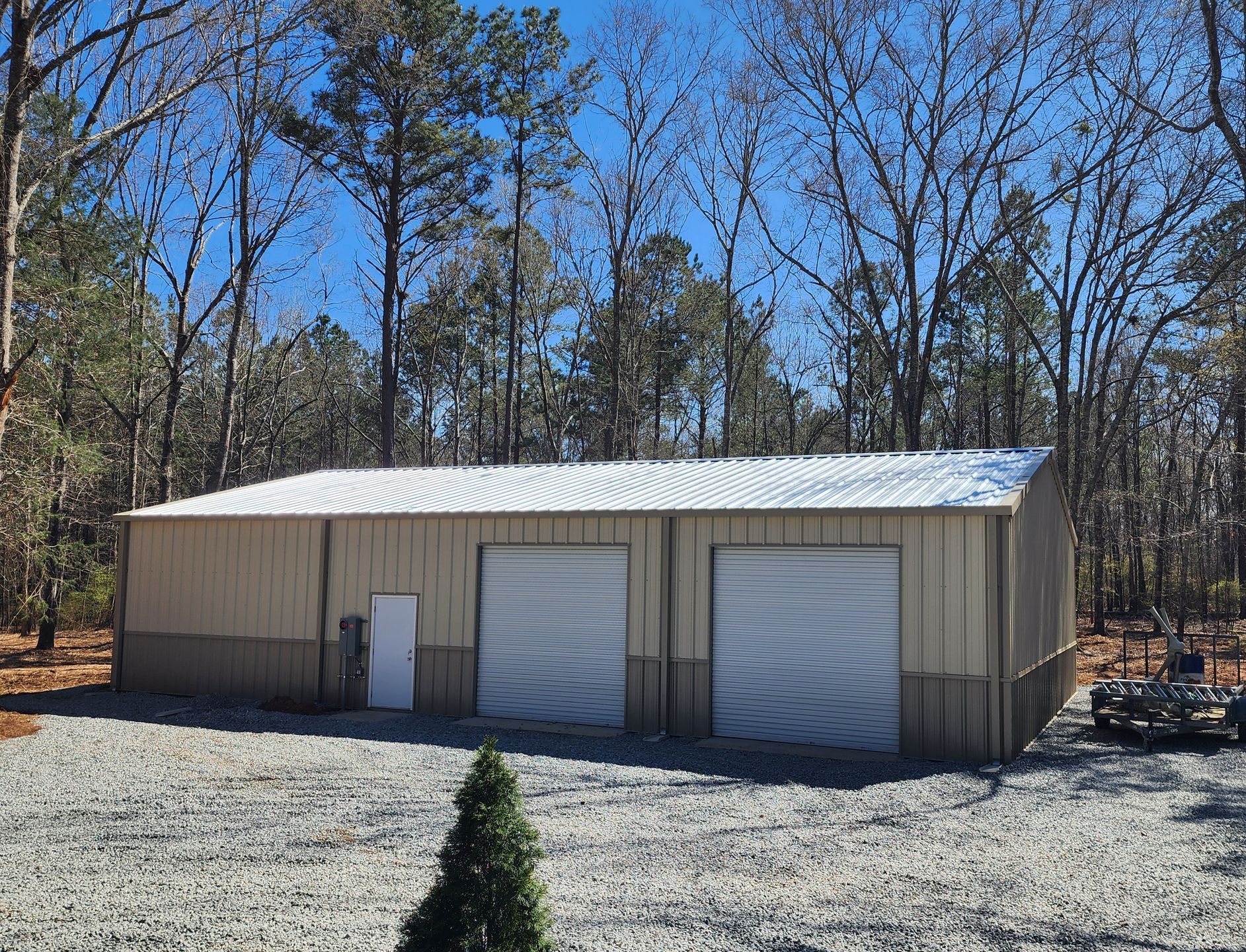 A large metal building with two garage doors is surrounded by trees.