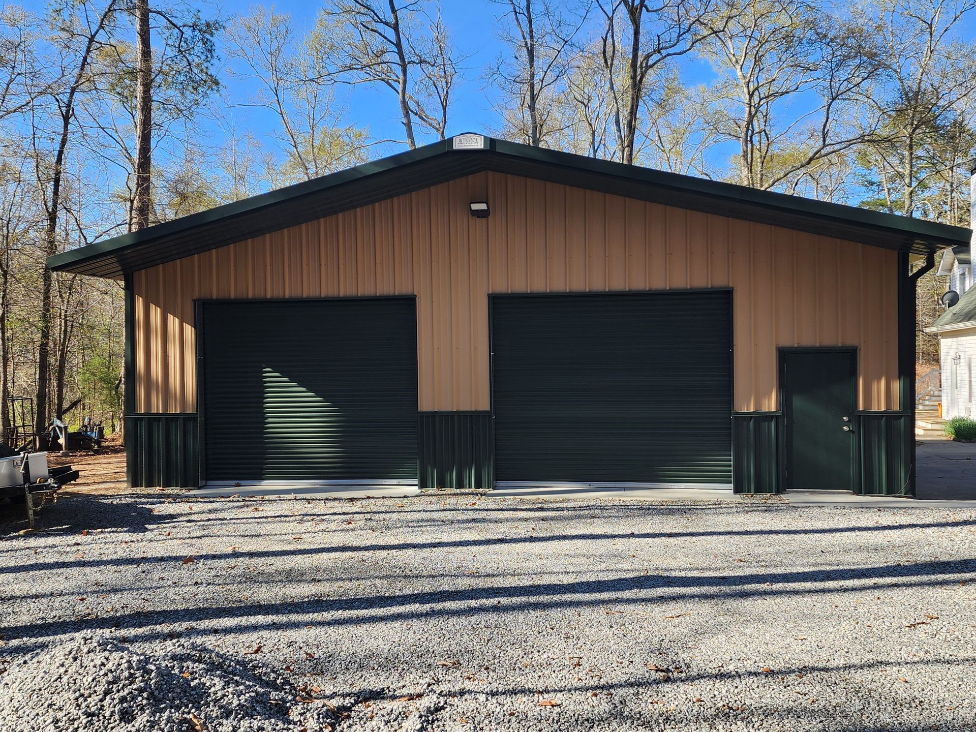 A large metal garage with three garage doors is sitting on top of a gravel driveway.
