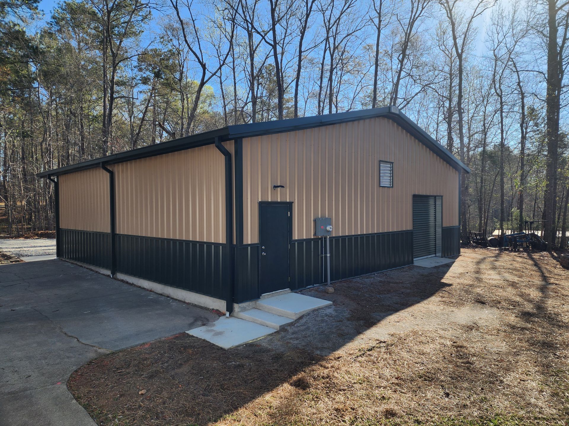 A large metal garage with three garage doors is sitting on top of a gravel driveway.