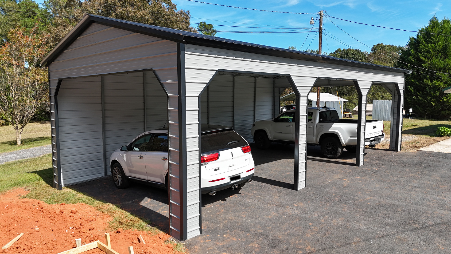 Gray metal carport with black trim; two SUVs and a truck parked inside.