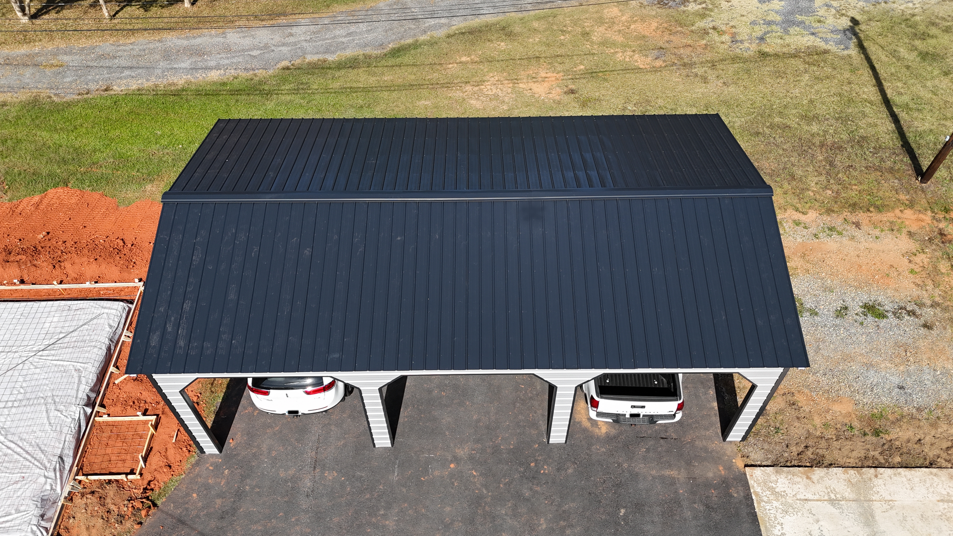 Metal carport with two parked vehicles on a concrete pad. Roof is black.