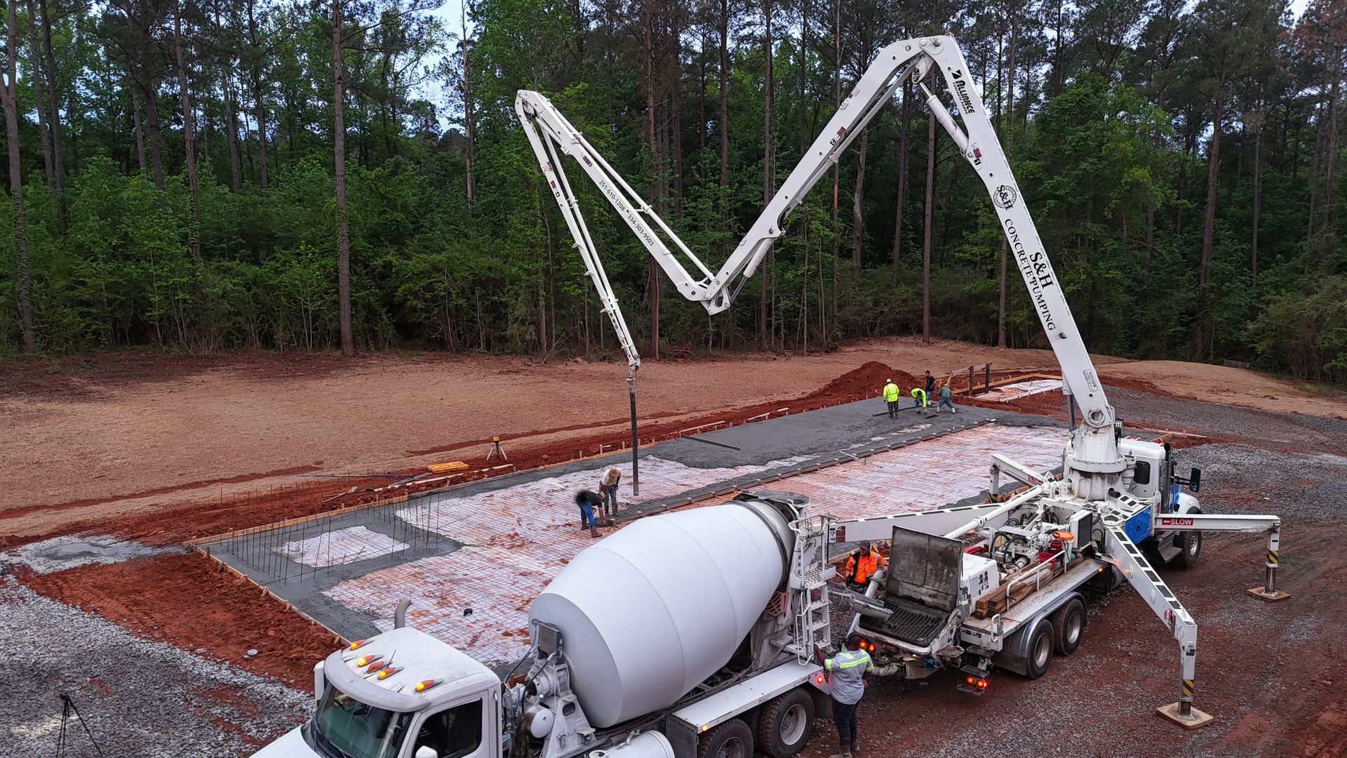Concrete mixer truck pumping white concrete through a long boom on a construction site