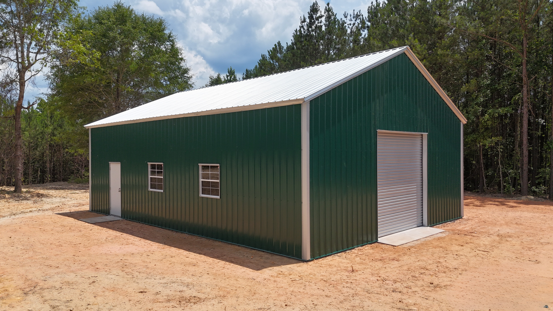 Green metal storage shed with white roof and open doorway on sandy ground near trees