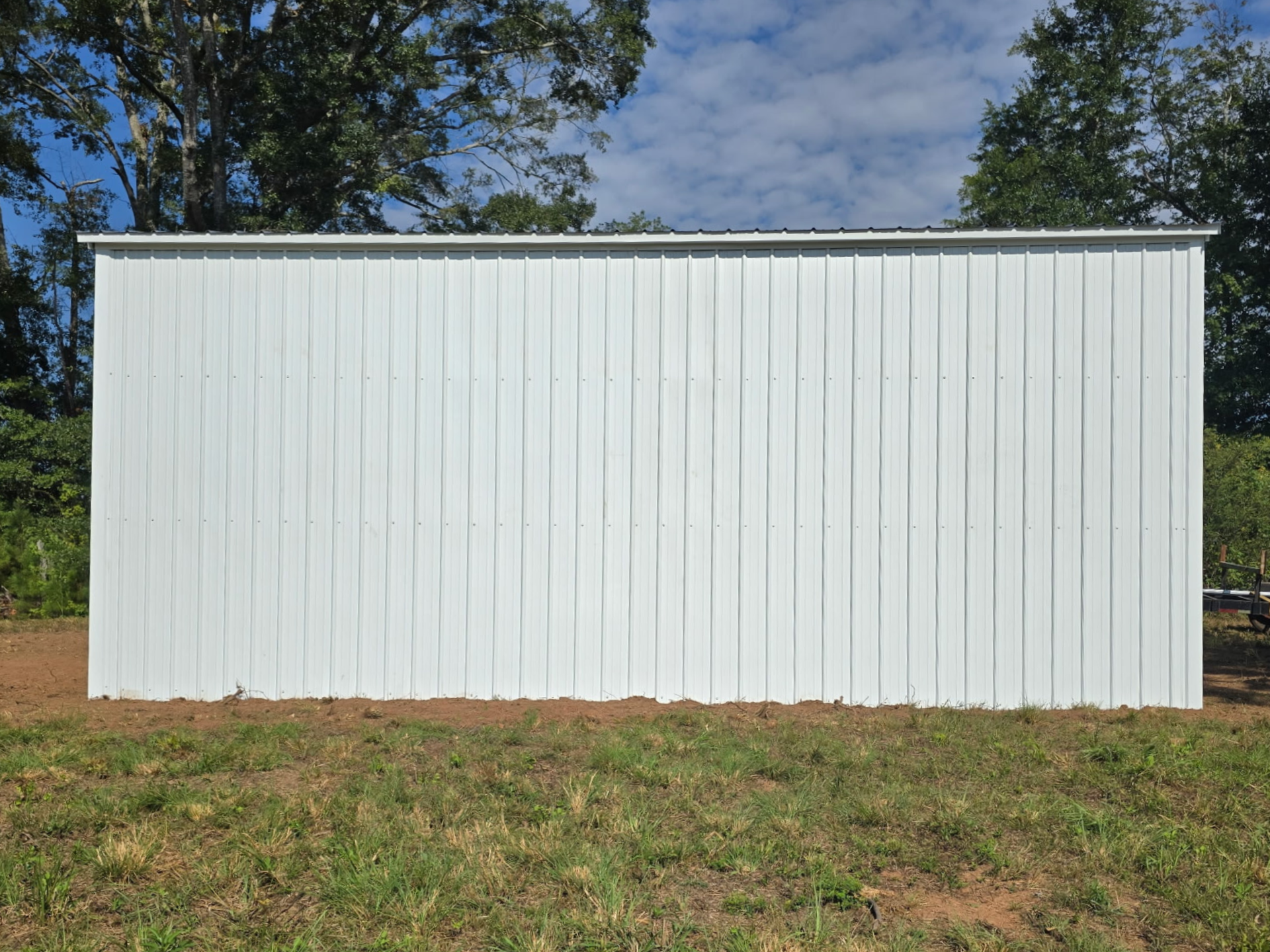White metal shed with a gray roof on a grassy lot under a blue sky.