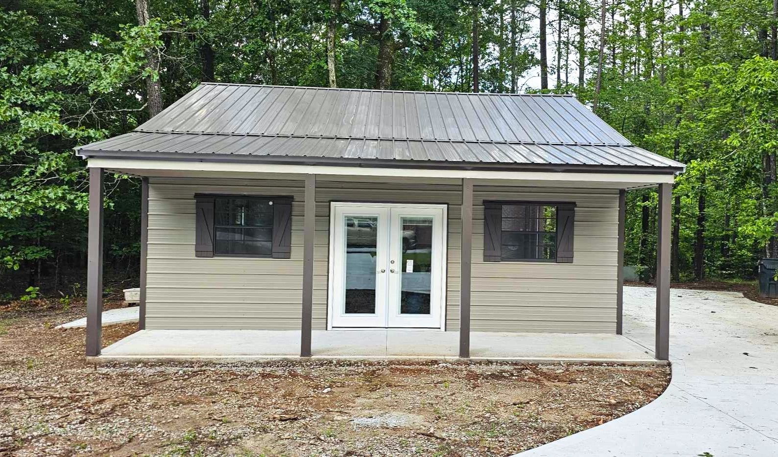 A small house with a porch and a metal roof is surrounded by trees.