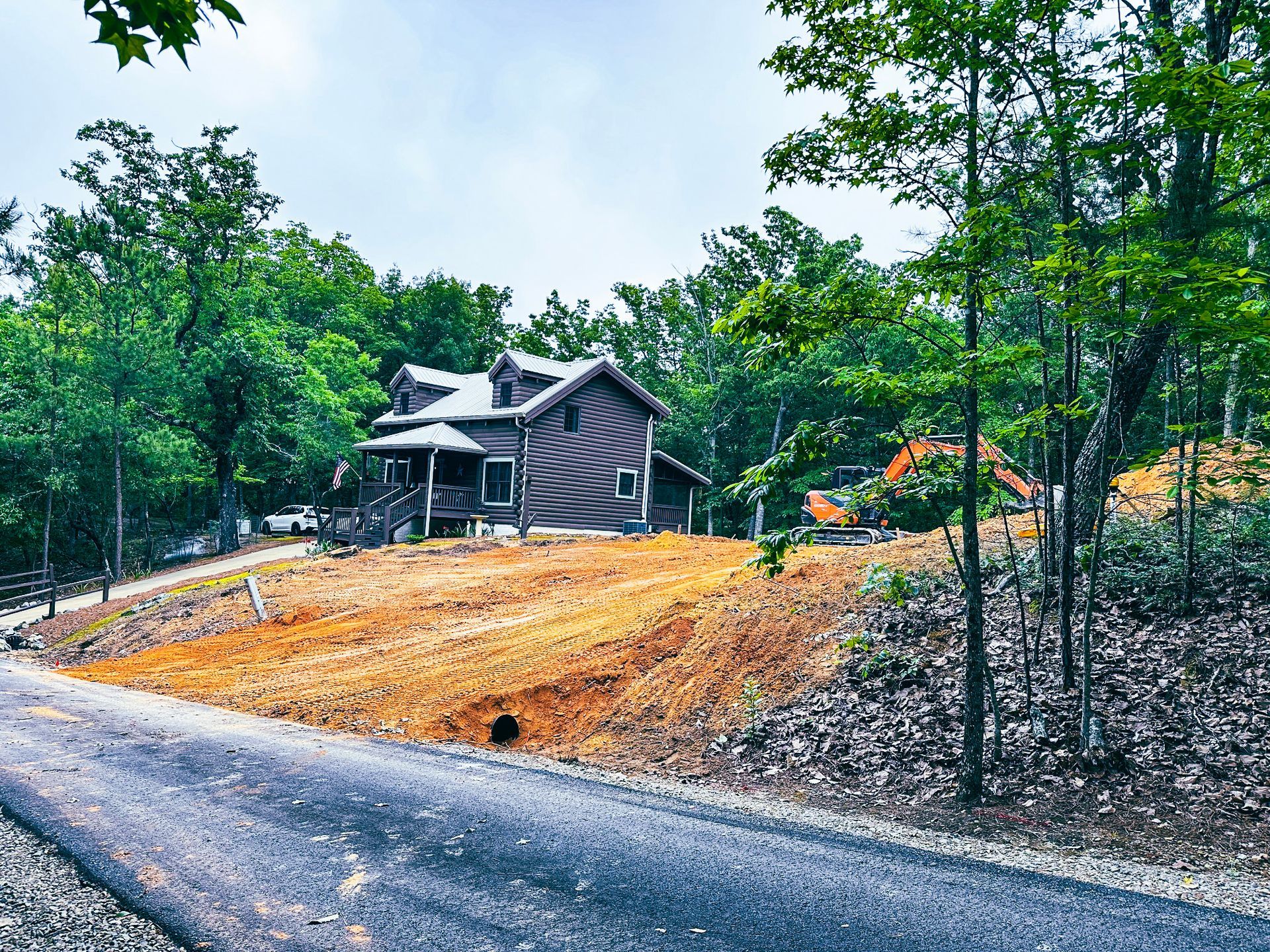 A house is sitting on top of a dirt hill in the middle of a forest.