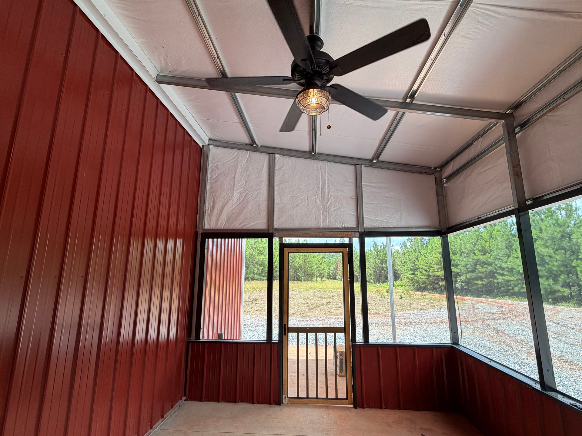 Covered porch with red paneled wall, screened windows, gate, and ceiling fan under a metal roof.