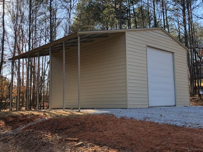 A garage with a canopy and a white door is sitting in the middle of a dirt field.