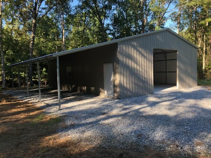 A large metal building with a canopy over it is in the middle of a forest.