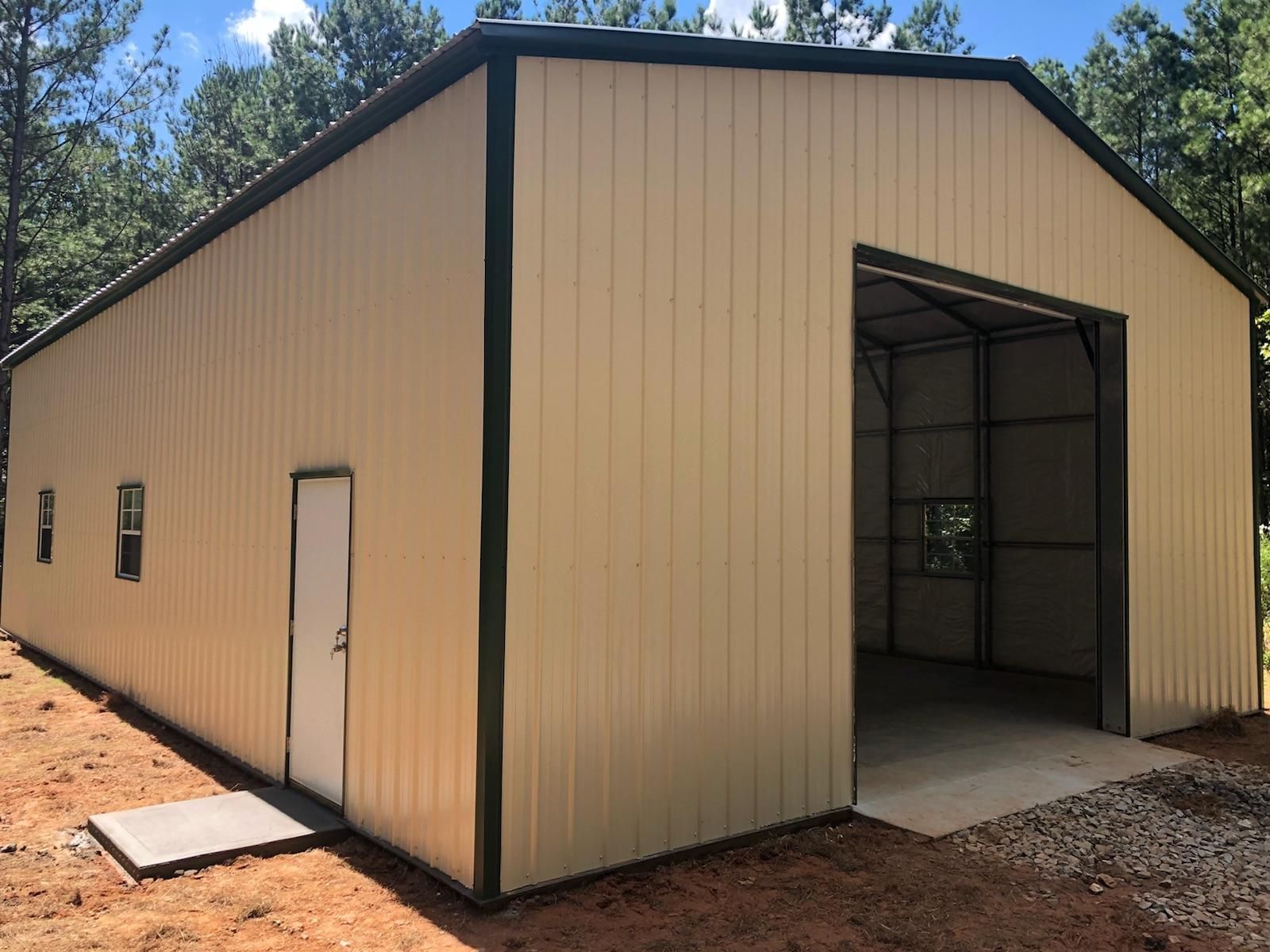 A large metal building with a door and windows is sitting on top of a dirt field.