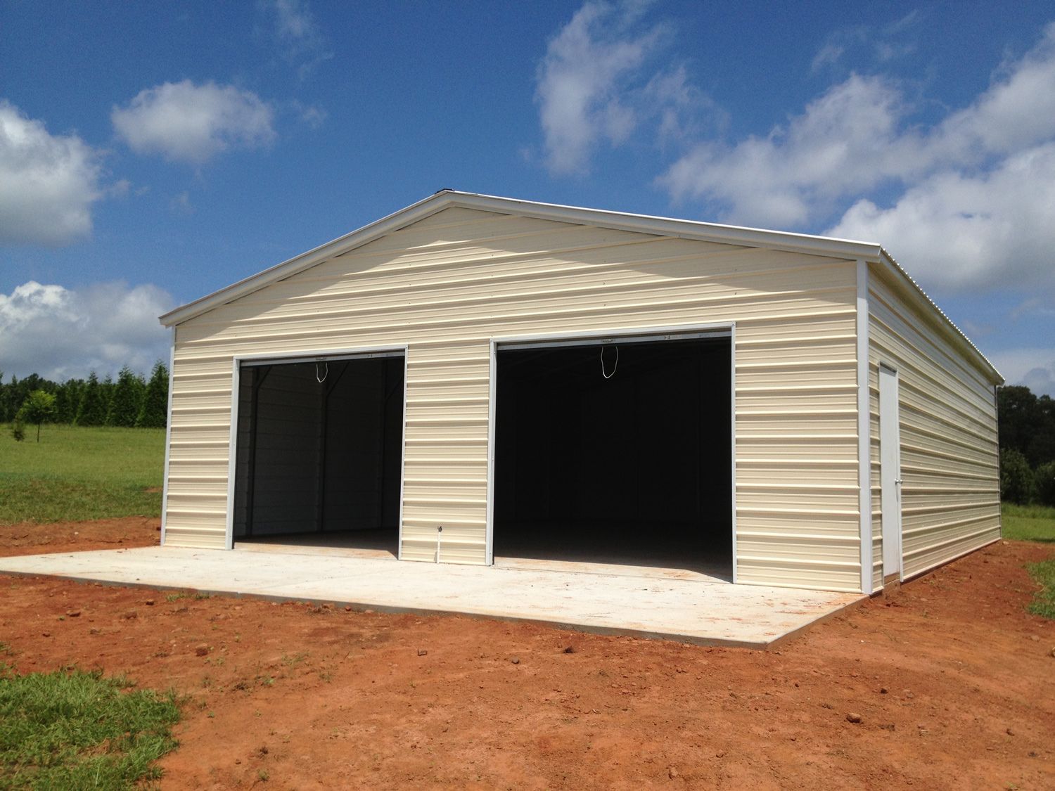 A white metal garage with two doors is sitting in the middle of a dirt field.