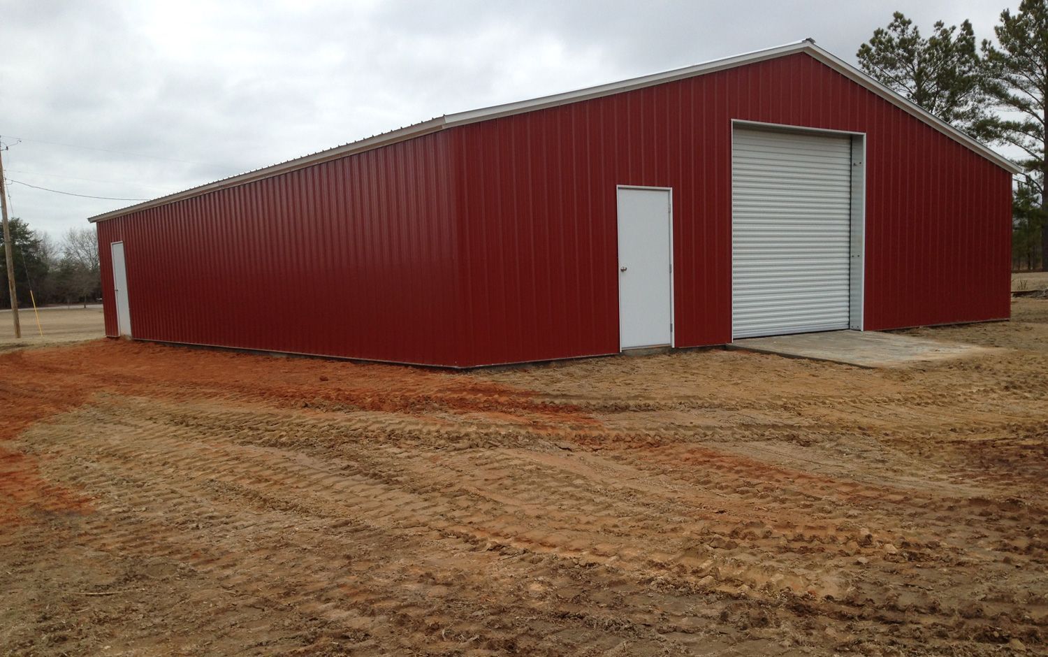 A large red barn with a white door is sitting in the middle of a dirt field.