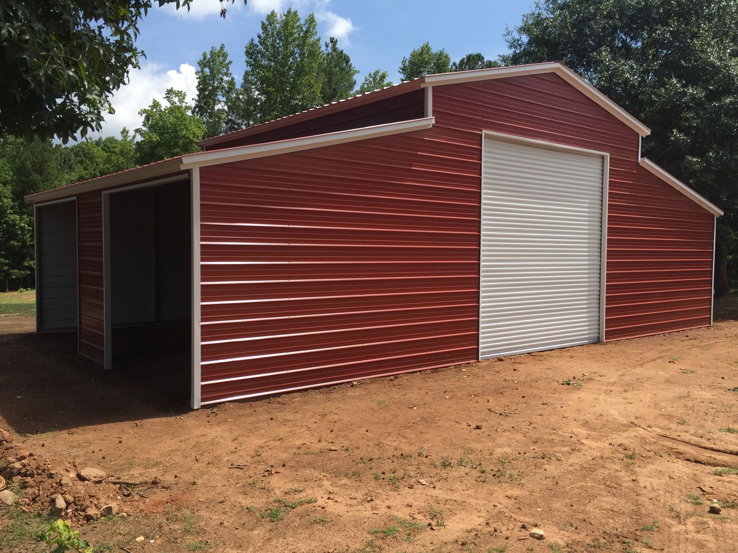 A red barn with a white door is in the middle of a dirt field.