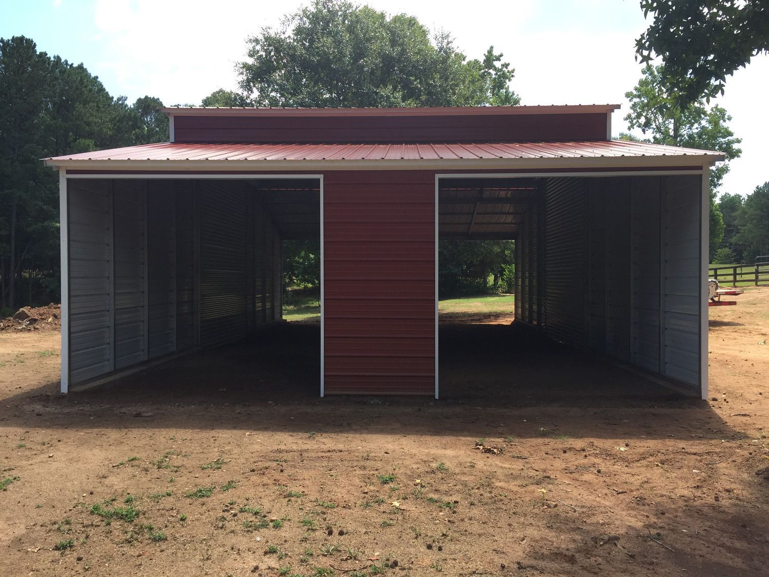 A red barn with a white roof is sitting in the middle of a dirt field.
