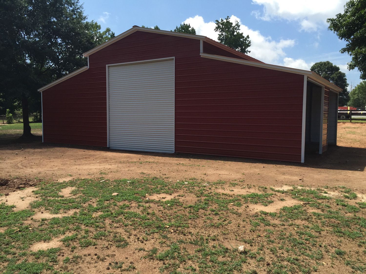 A red barn with a white door is sitting in the middle of a grassy field.