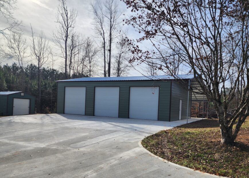 A garage with three garage doors and a tree in front of it.
