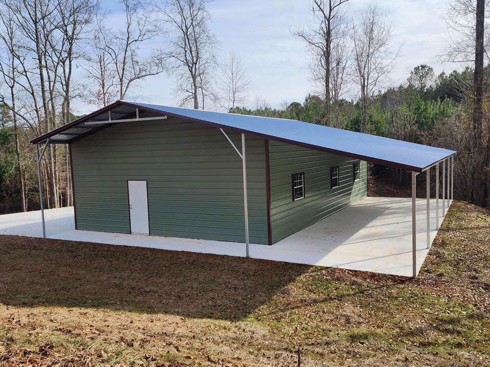 A green metal building with a blue roof is sitting in the middle of a field.