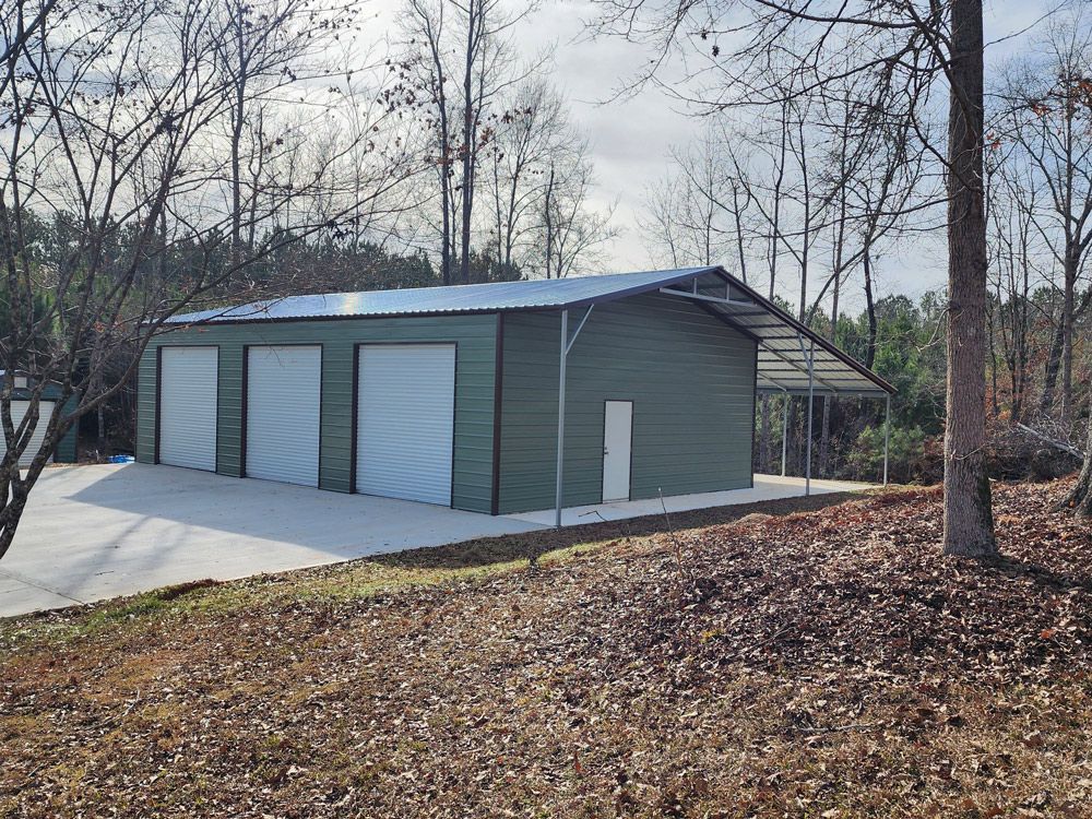 A green garage with white doors is sitting on top of a hill next to trees.
