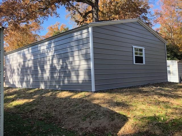 A gray garage with a window and a tree in the background.