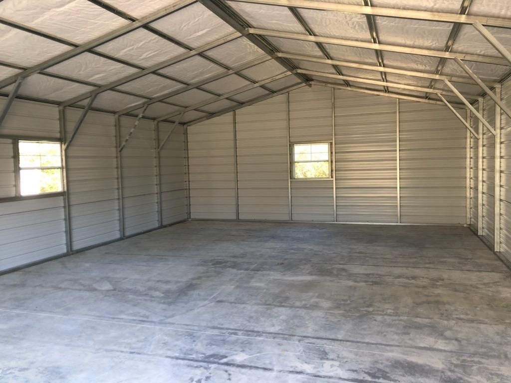 A large empty metal garage with a concrete floor and windows.