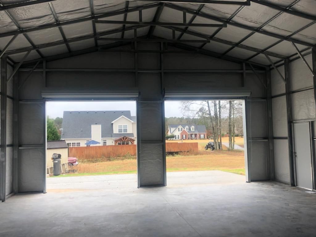 The inside of a garage with the doors open and a house in the background.