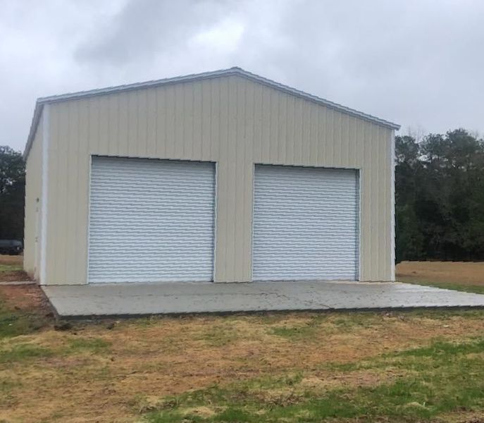 A garage with two garage doors is sitting in the middle of a grassy field.