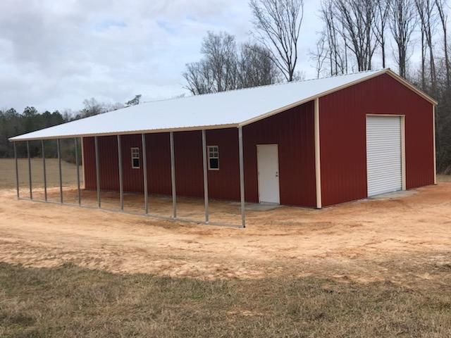 A red barn with a white roof is sitting in the middle of a dirt field.