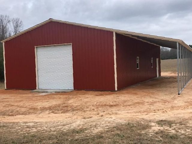 A red barn with a white door is sitting in the middle of a dirt field.