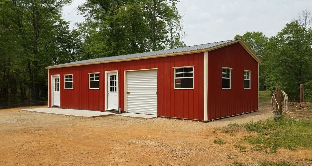 A red barn with white doors and windows is sitting in the middle of a dirt field.