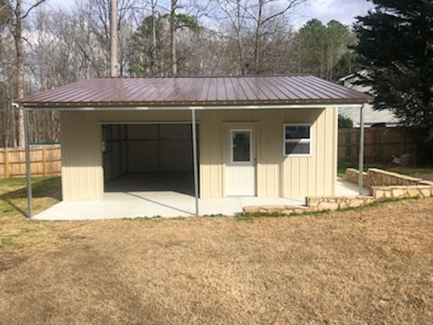 A small garage with a brown roof is sitting in the middle of a grassy field.