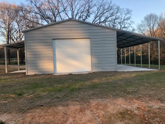 A metal garage with a carport attached to it in a field.