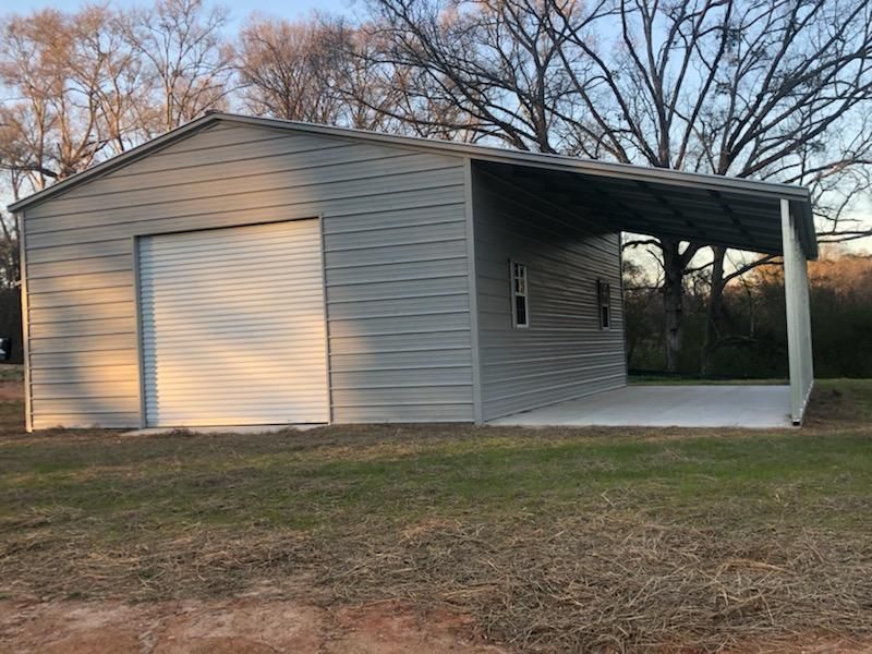 A garage with a canopy and a driveway in a field.