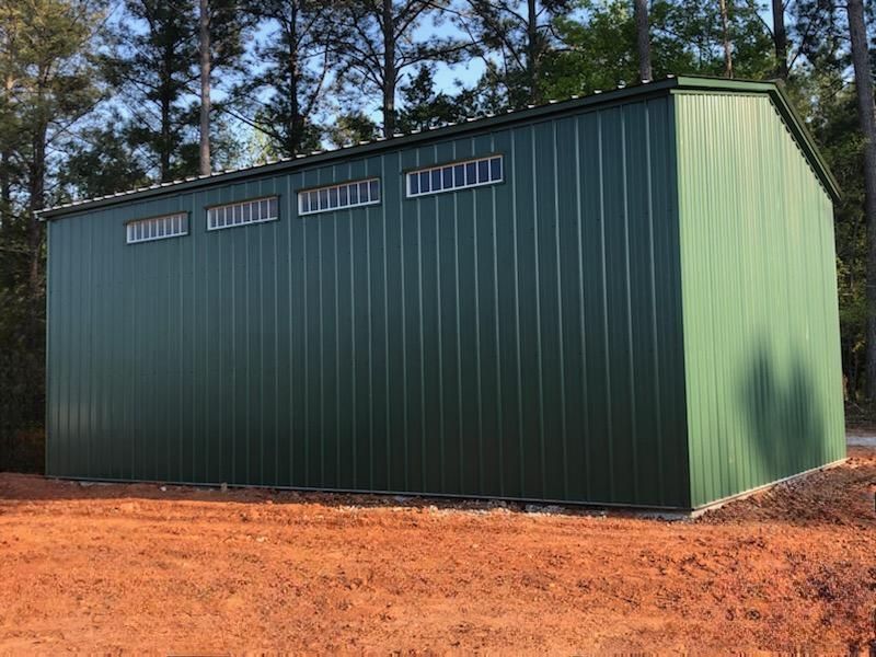 A green metal building is sitting in the middle of a dirt field.