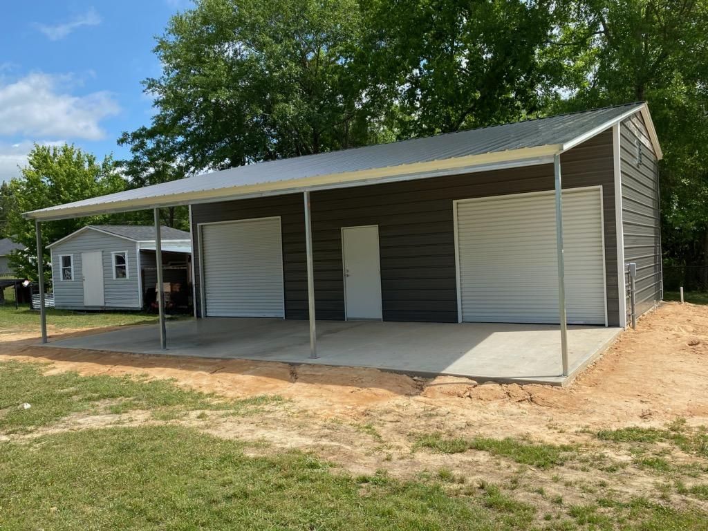 A garage with a canopy over it is sitting in the middle of a grassy field.
