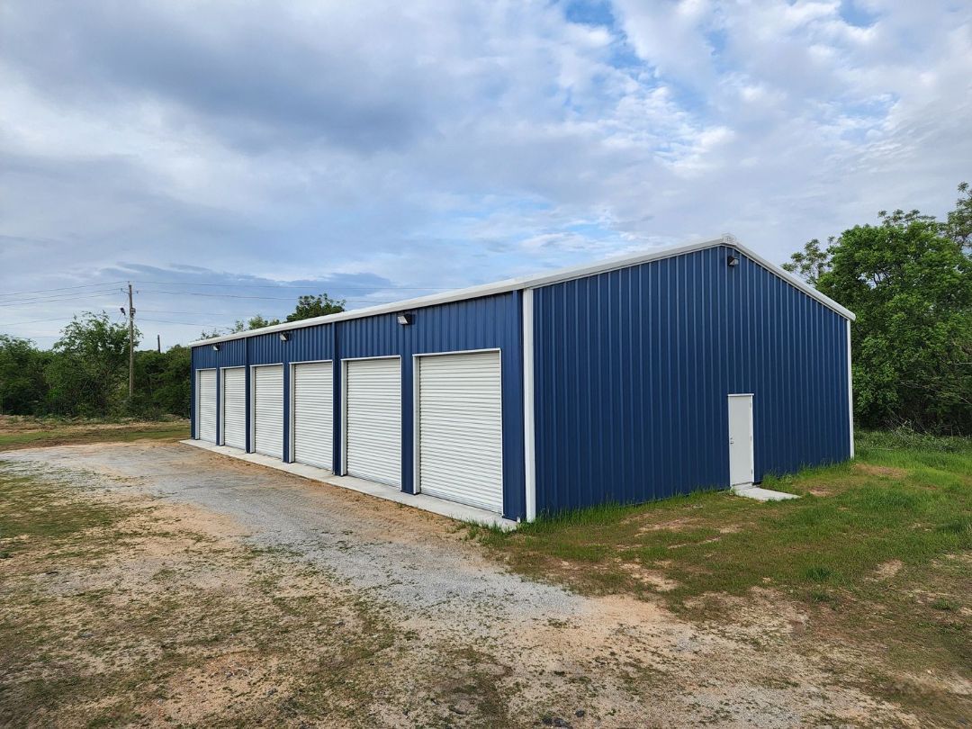 A blue metal building with white doors is sitting on top of a dirt field.