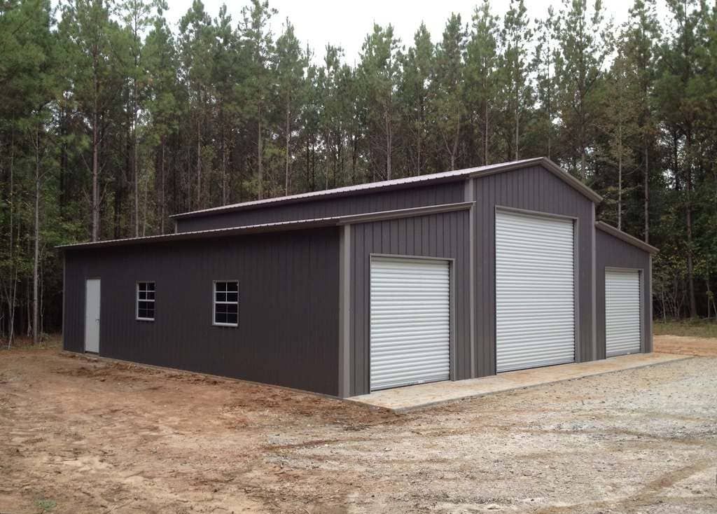 A large metal building with two garage doors is in the middle of a forest.