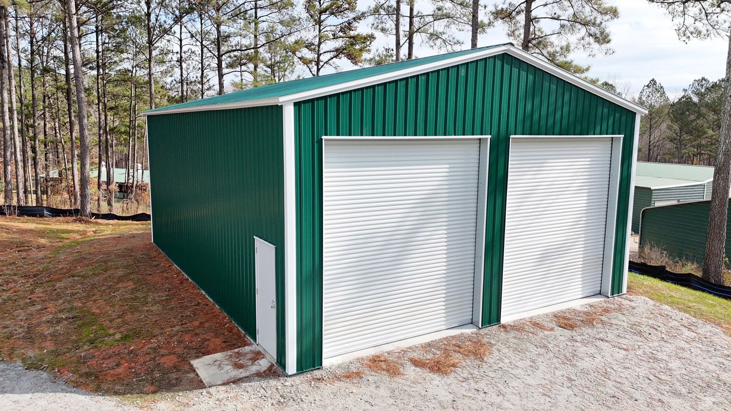 A green and white garage with two garage doors is sitting on top of a gravel road.