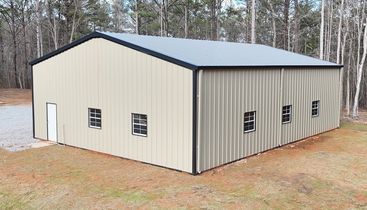 A large metal building with a black roof is sitting in the middle of a field.