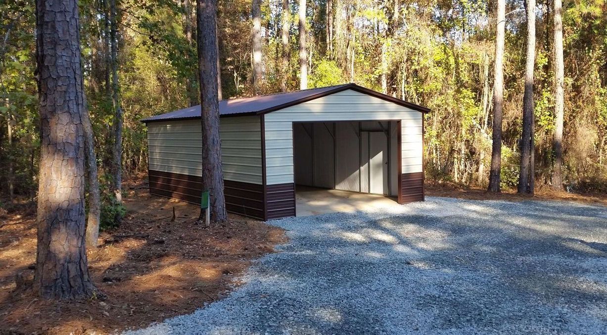 A garage is sitting in the middle of a gravel driveway in the woods.